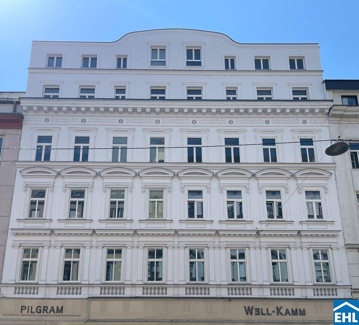 Die weiße Fassade des Gebäudes mit vielen Fenstern und klassischer Architektur, die auf eine Renovierung hindeutet.