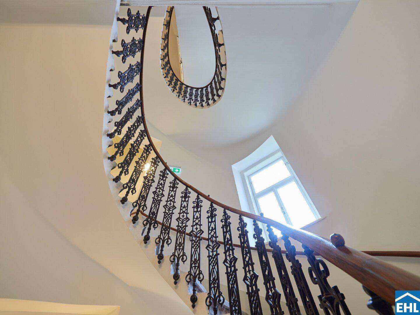 Elegantes, spiralförmiges Treppenhaus mit kunstvollem Geländer und hellem Lichteinfall von oben.