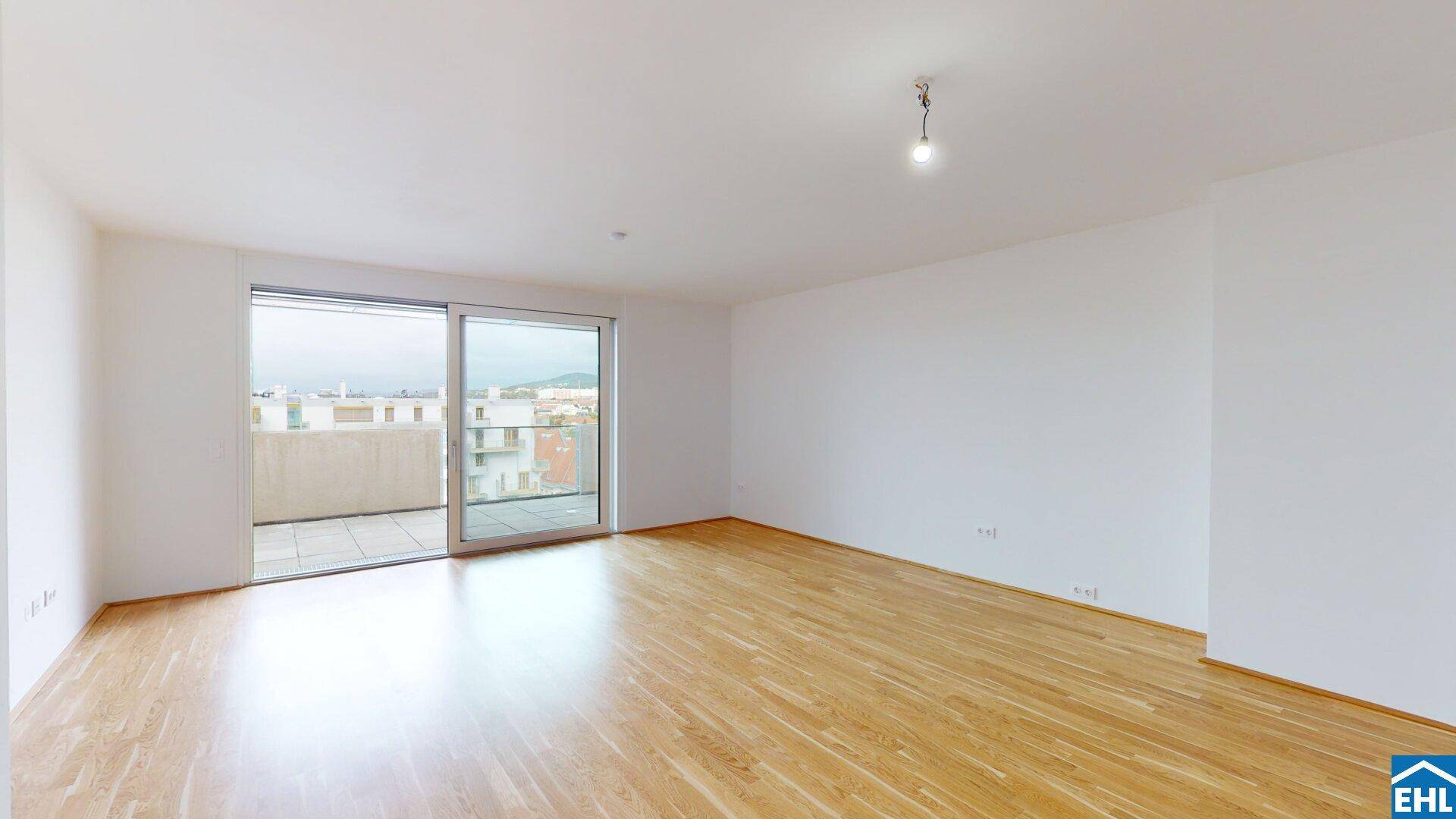 Helles, leeres Wohnzimmer mit Holzboden und großen Schiebetüren, die zu einer Terrasse führen.