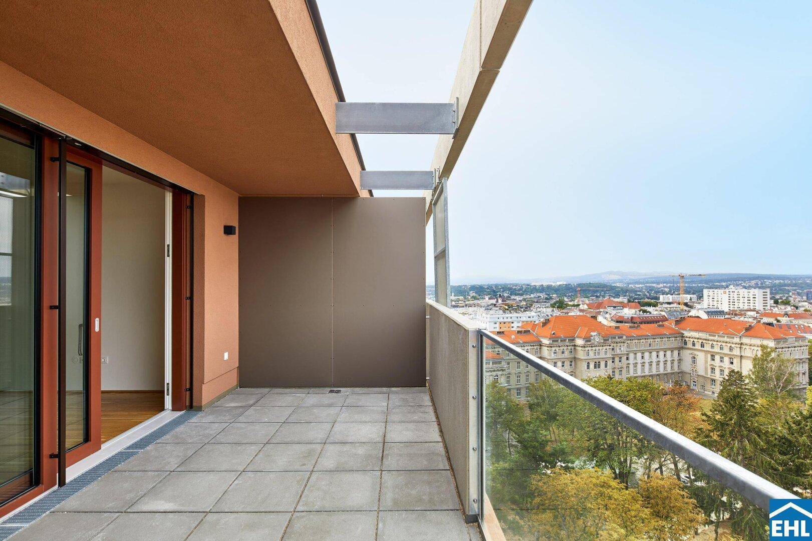 Breiter Balkon mit Glasgeländer und Panoramablick auf die umliegende Stadt und die Hügel im Hintergrund.