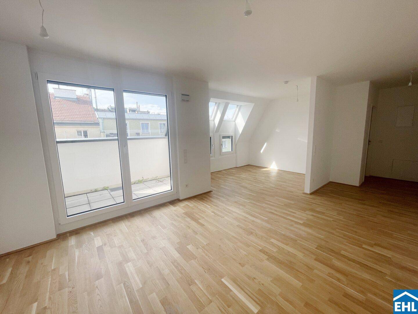 Helles Wohnzimmer mit Holzboden, großen Fenstern und Zugang zu einem Balkon im Dachgeschoss.