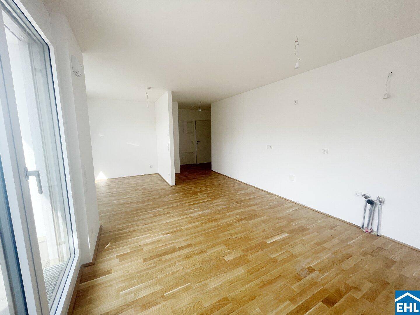 Großzügiger, leerer Wohnraum mit Holzboden und einem Durchgang zu weiteren Zimmern.