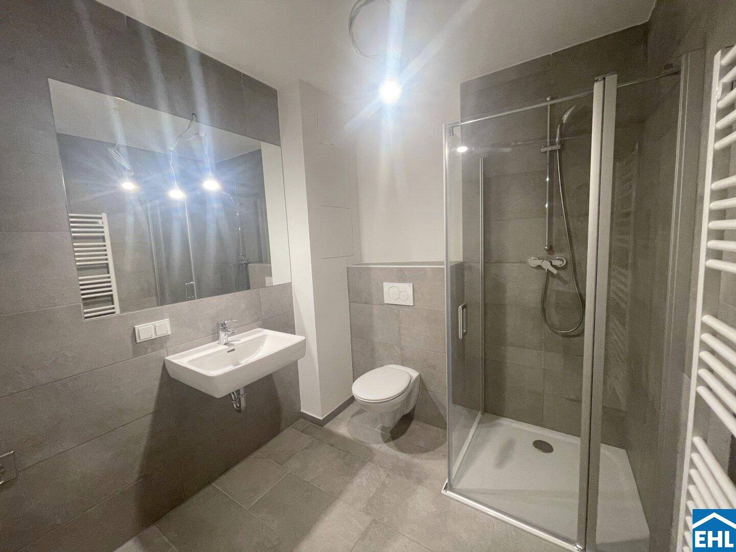 Modernes Badezimmer mit grauen Fliesen, Dusche und wandhängendem WC.