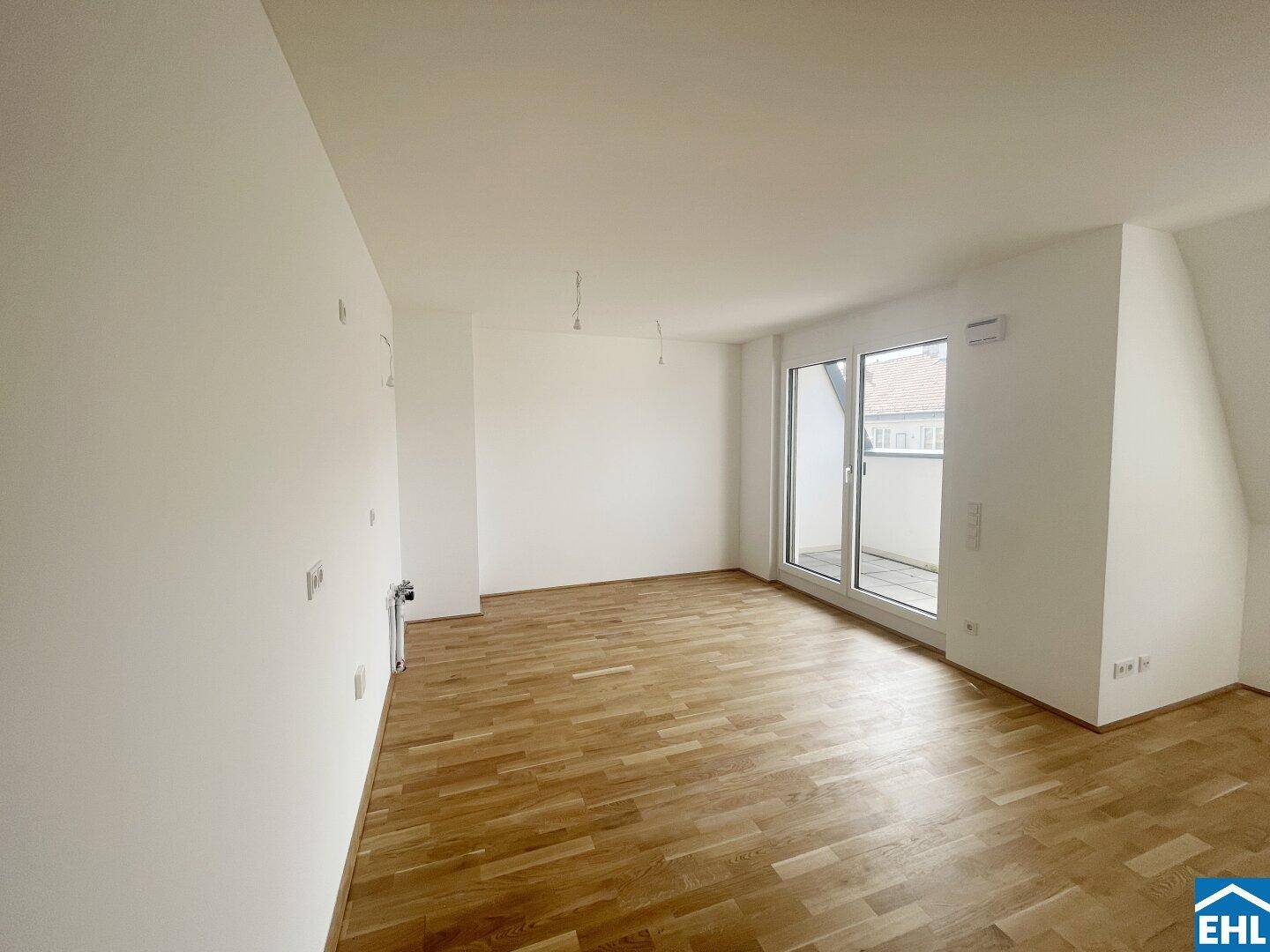 Geräumiges, leeres Wohnzimmer mit Holzboden und Zugang zu einem kleinen Balkon.