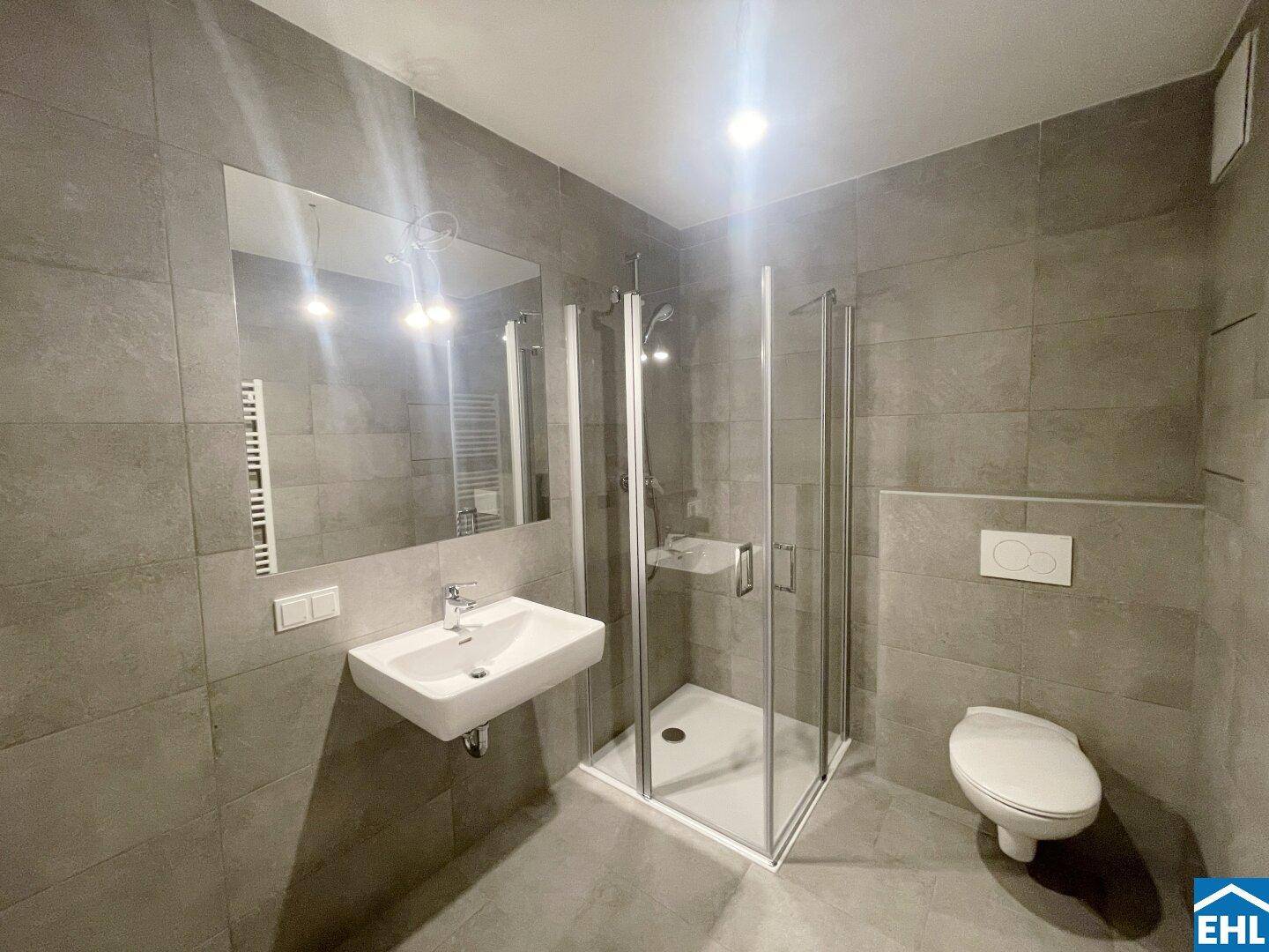 Modernes Badezimmer mit grauen Fliesen, Duschkabine, wandhängendem WC und Handtuchheizkörper.