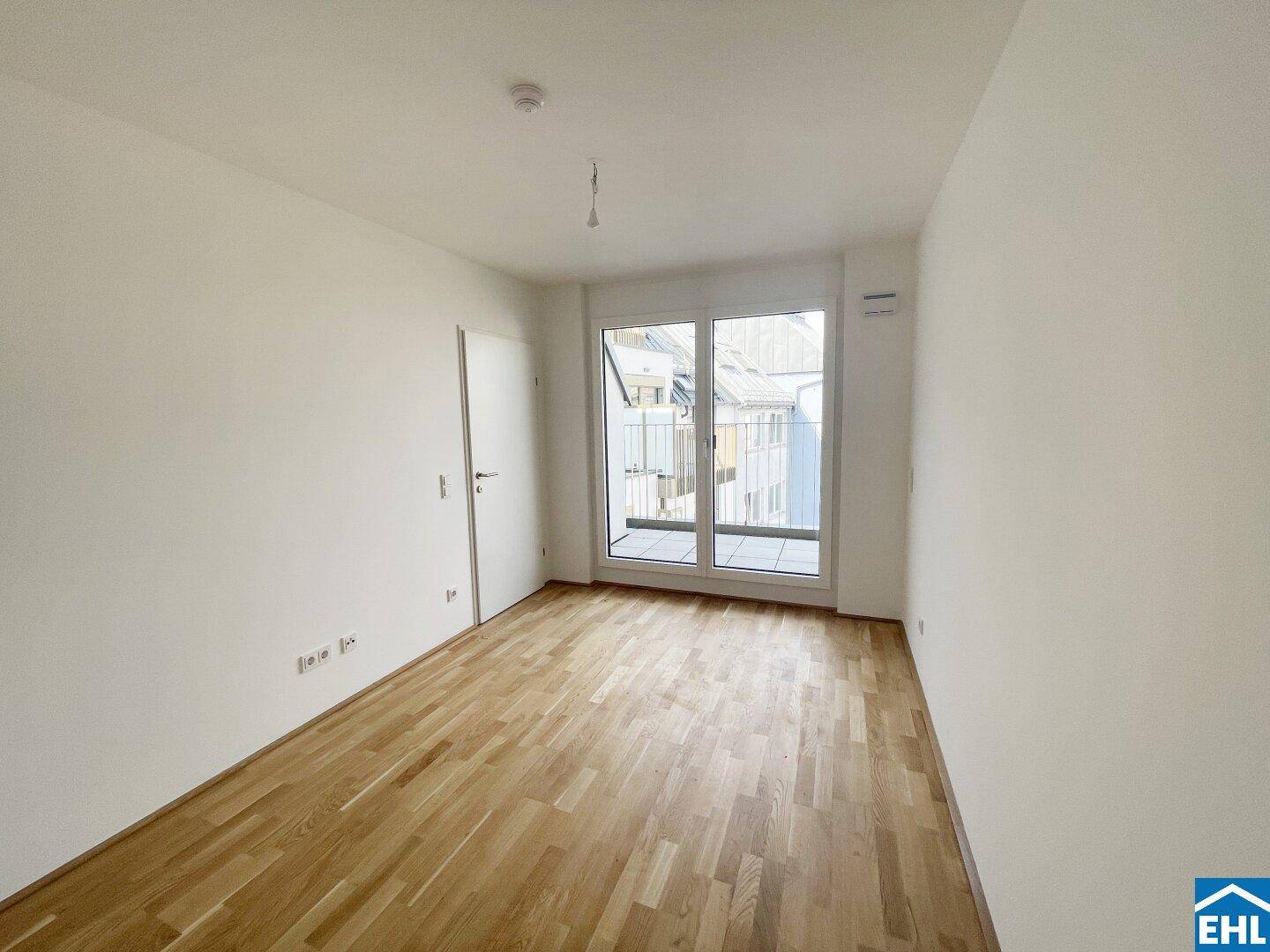 Helles Zimmer mit Parkettboden und Zugang zu einem kleinen Balkon, ideal als Schlafzimmer.