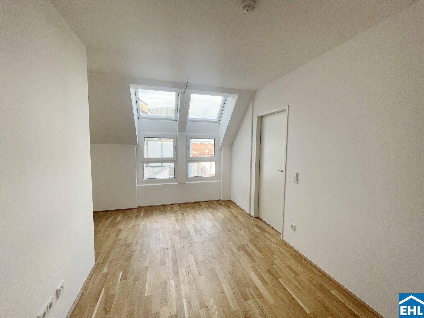 Lichtdurchflutetes Dachzimmer mit Parkettboden und mehreren Dachfenstern, schafft eine helle Wohnatmosphäre.