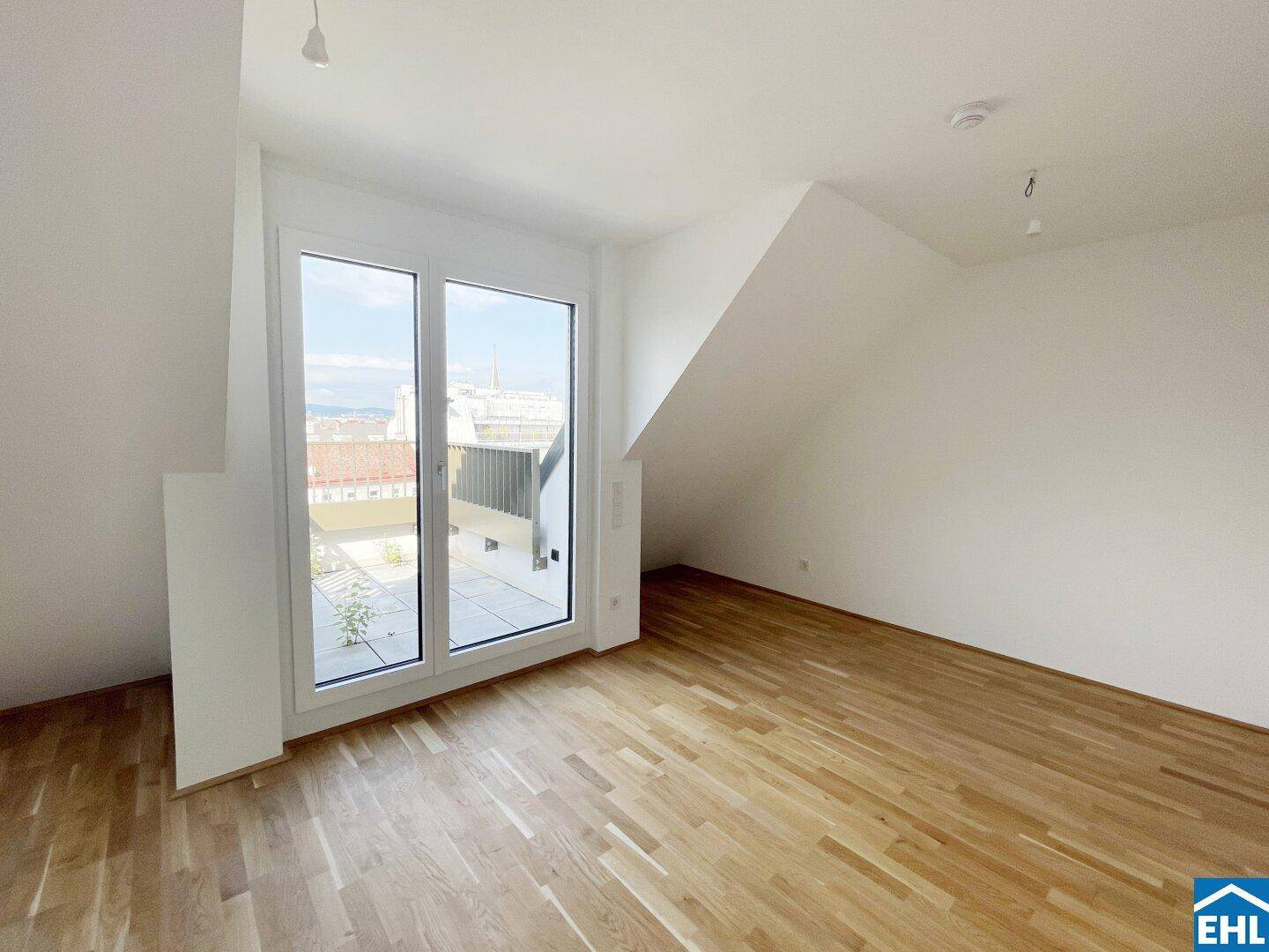 Heller Dachgeschossraum mit Holzboden, schrägen Wänden und Zugang zu einer kleinen Terrasse.