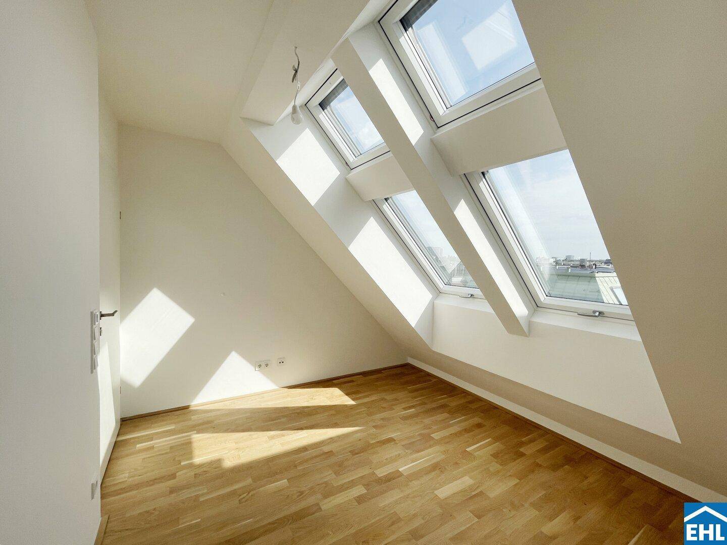 Lichtdurchfluteter Dachgeschossraum mit Holzboden und mehreren großen Dachfenstern.