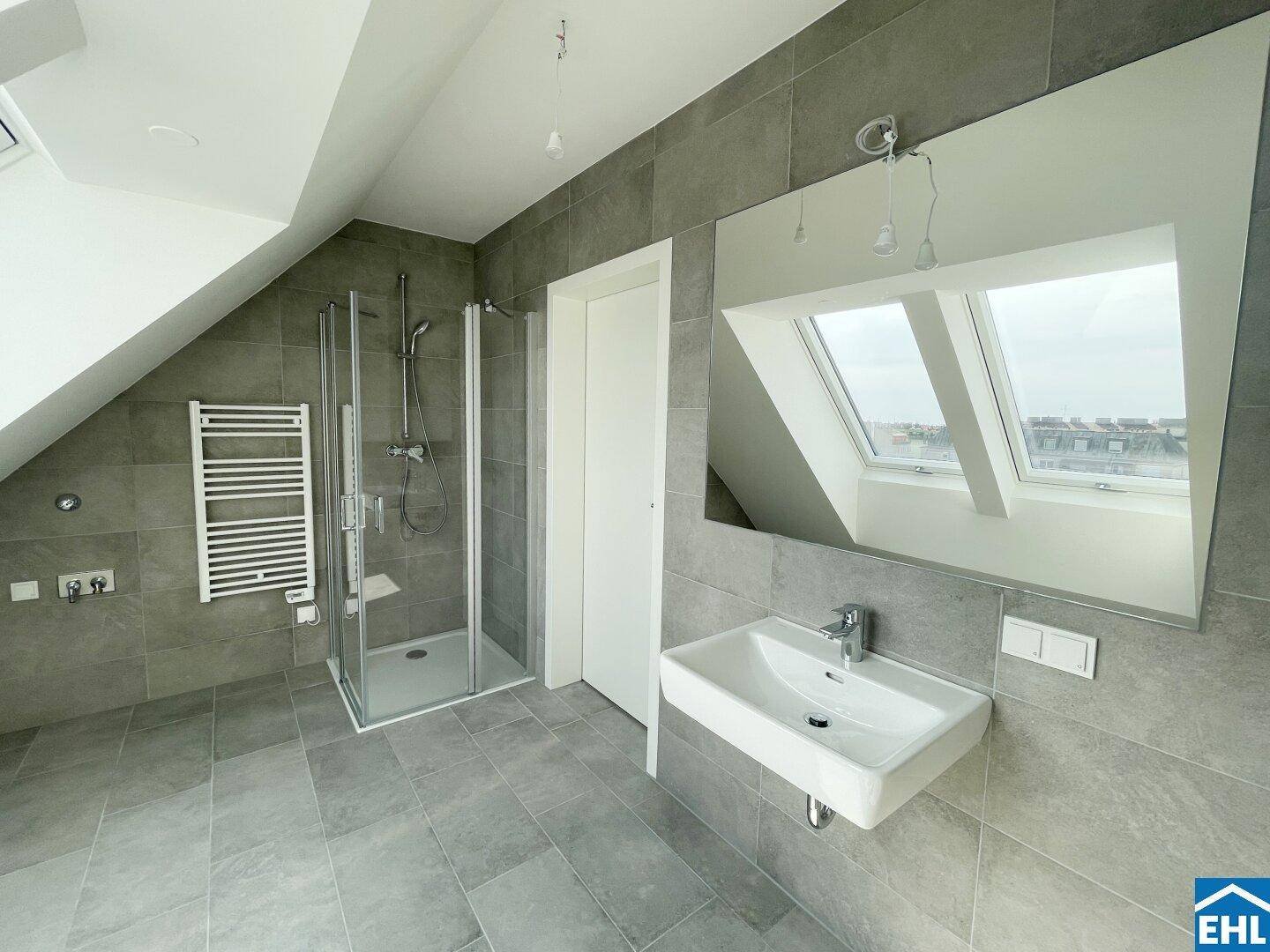 Modernes Badezimmer mit grauen Fliesen, Duschkabine und beheiztem Handtuchhalter im Dachgeschoss.