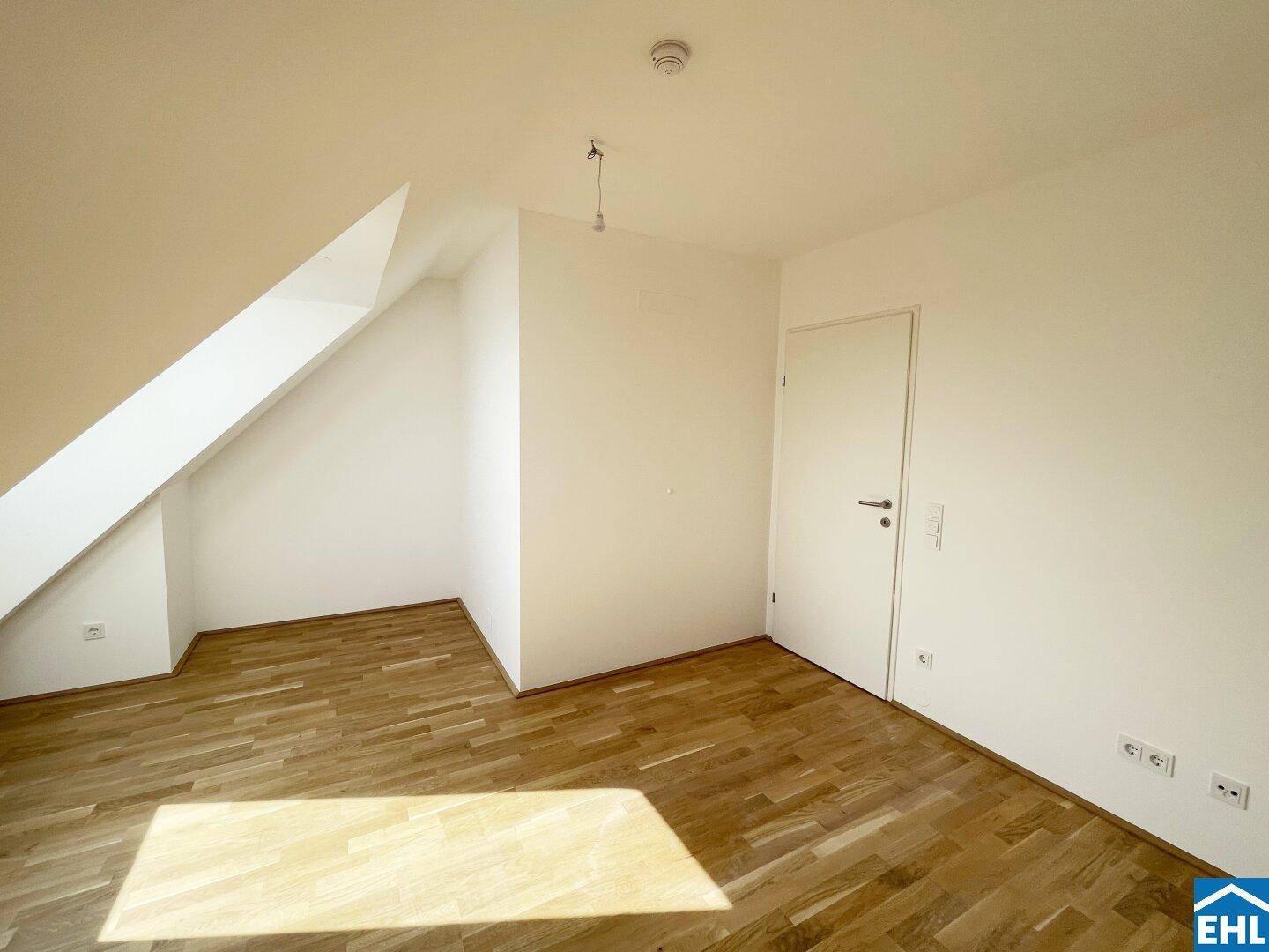 Heller Dachgeschossraum mit Holzboden und weißen Wänden, ideal für ein Schlafzimmer oder Büro.