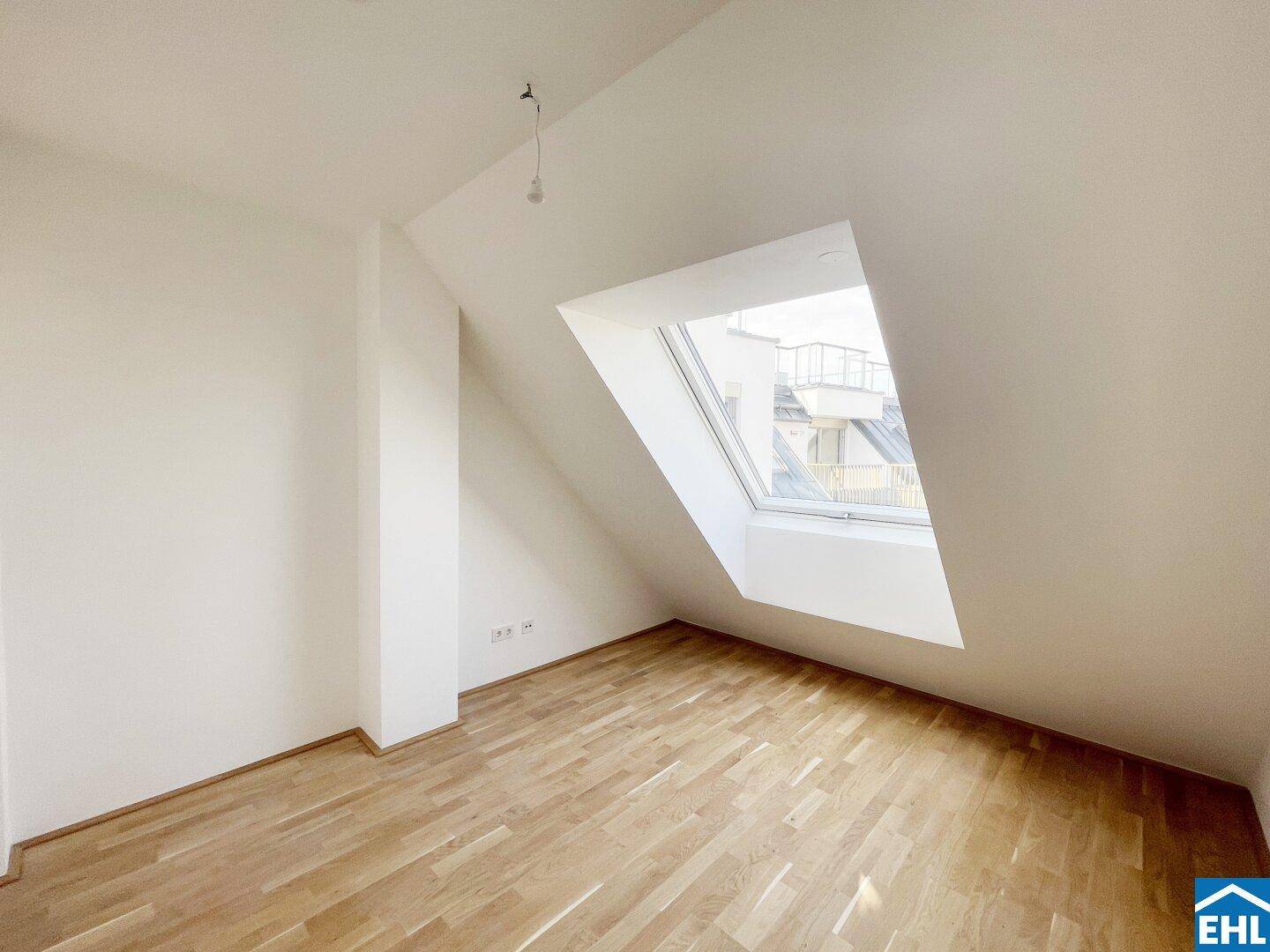 Heller Dachgeschossraum mit Holzboden und einem großen Dachfenster, das den Raum mit Licht füllt.