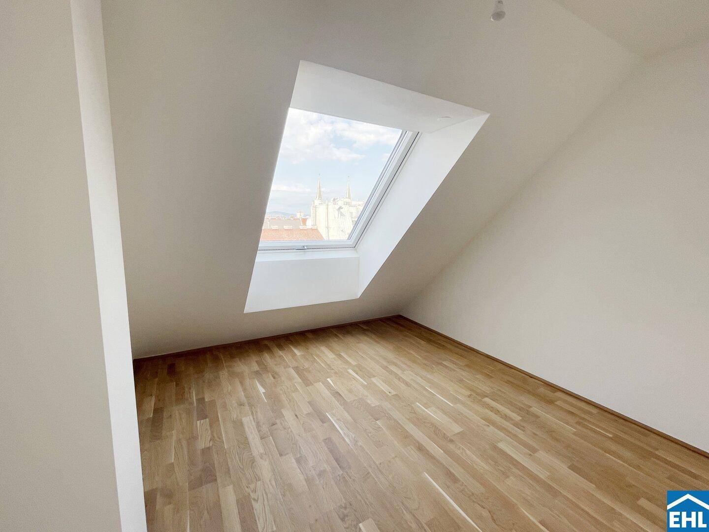Ruhiger Dachgeschossraum mit Holzboden und einem großen Dachfenster, das den Raum erhellt.