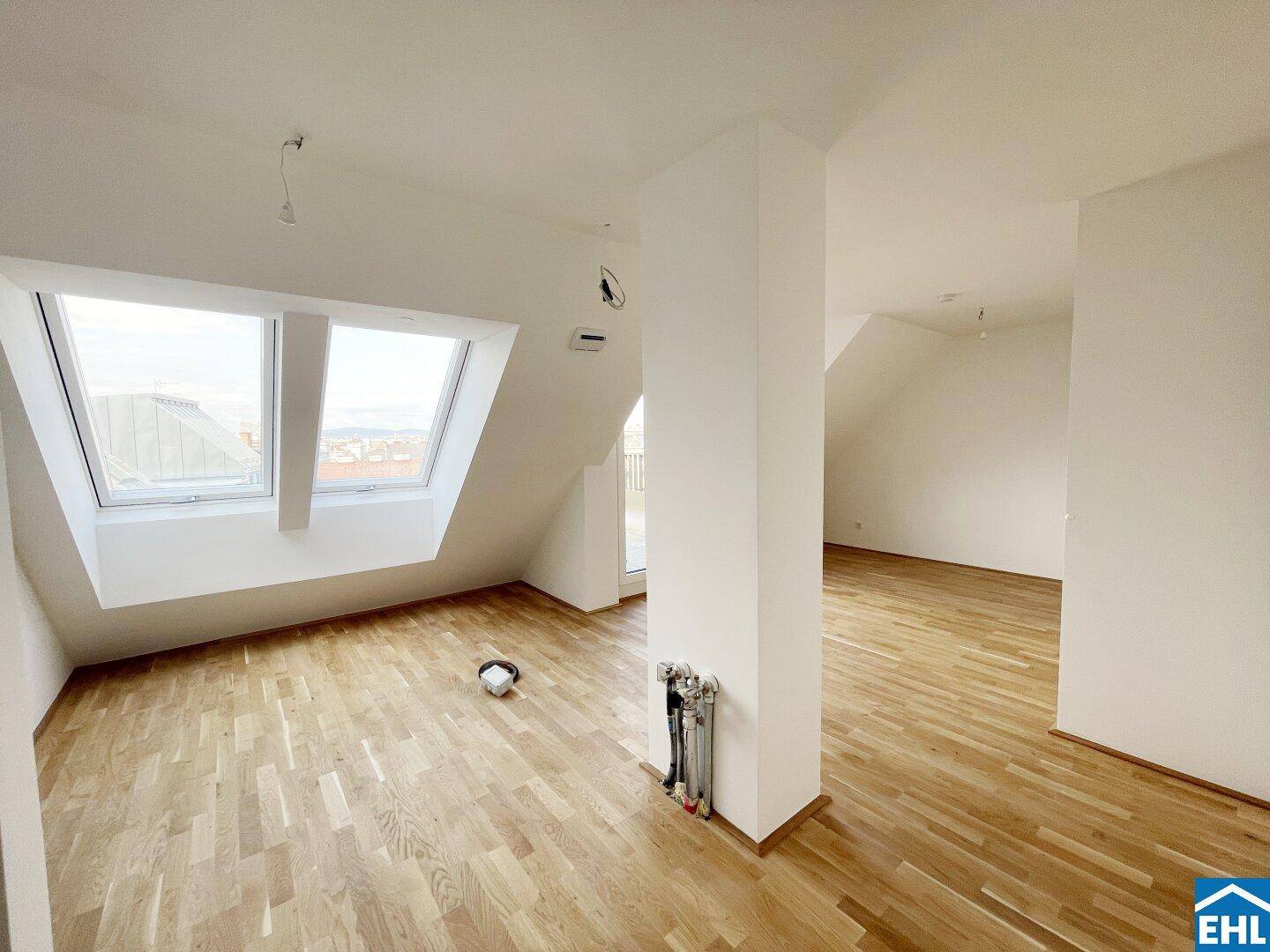 Heller Dachgeschossraum mit Holzboden, weißen Wänden und großen Dachfenstern, die viel Licht hereinlassen.