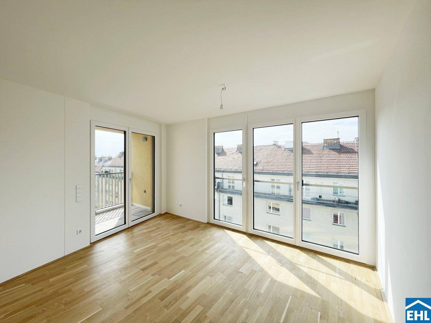 Helles Zimmer mit Parkettboden, großen Fenstern und Zugang zu einem Balkon mit Stadtblick.