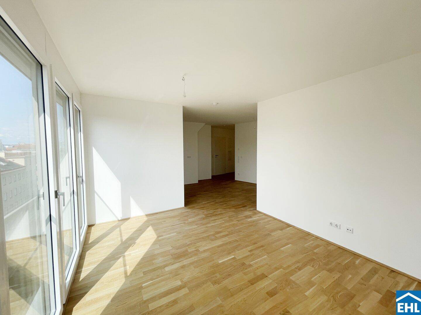 Geräumiges, helles Zimmer mit Holzboden und großen Fenstern, die viel Tageslicht hereinlassen.