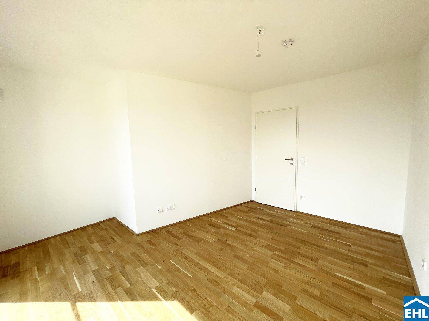 Leeres Zimmer mit hellem Parkettboden und weiß gestrichenen Wänden, bereit zur individuellen Gestaltung.