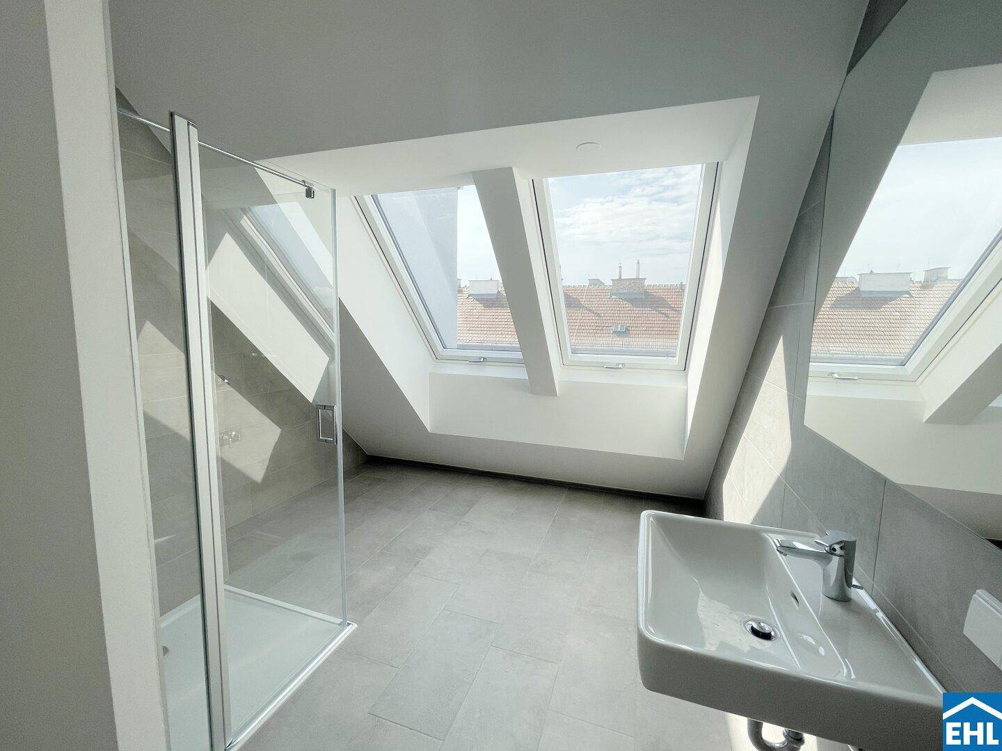 Helles Badezimmer im Dachgeschoss mit modernen Fliesen, Dusche und zwei Dachfenstern.