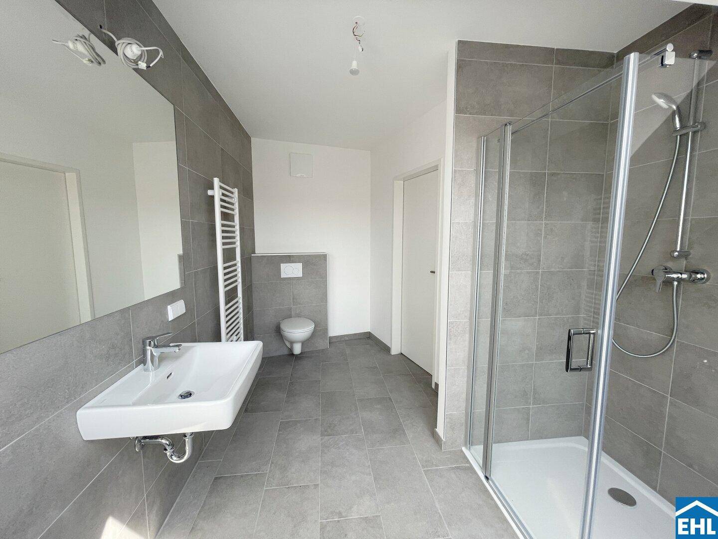 Modernes Badezimmer mit grauen Fliesen, Einzelwaschbecken, Toilette und einer geräumigen Dusche.