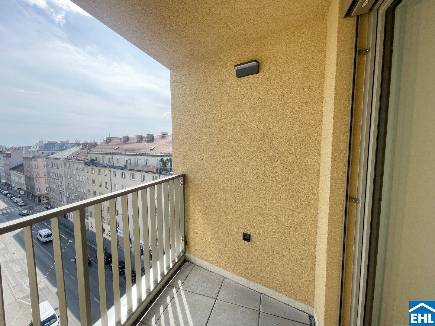 Balkon mit gelber Fassade und Blick auf die darunterliegende Stadtstraße und umliegende Gebäude.