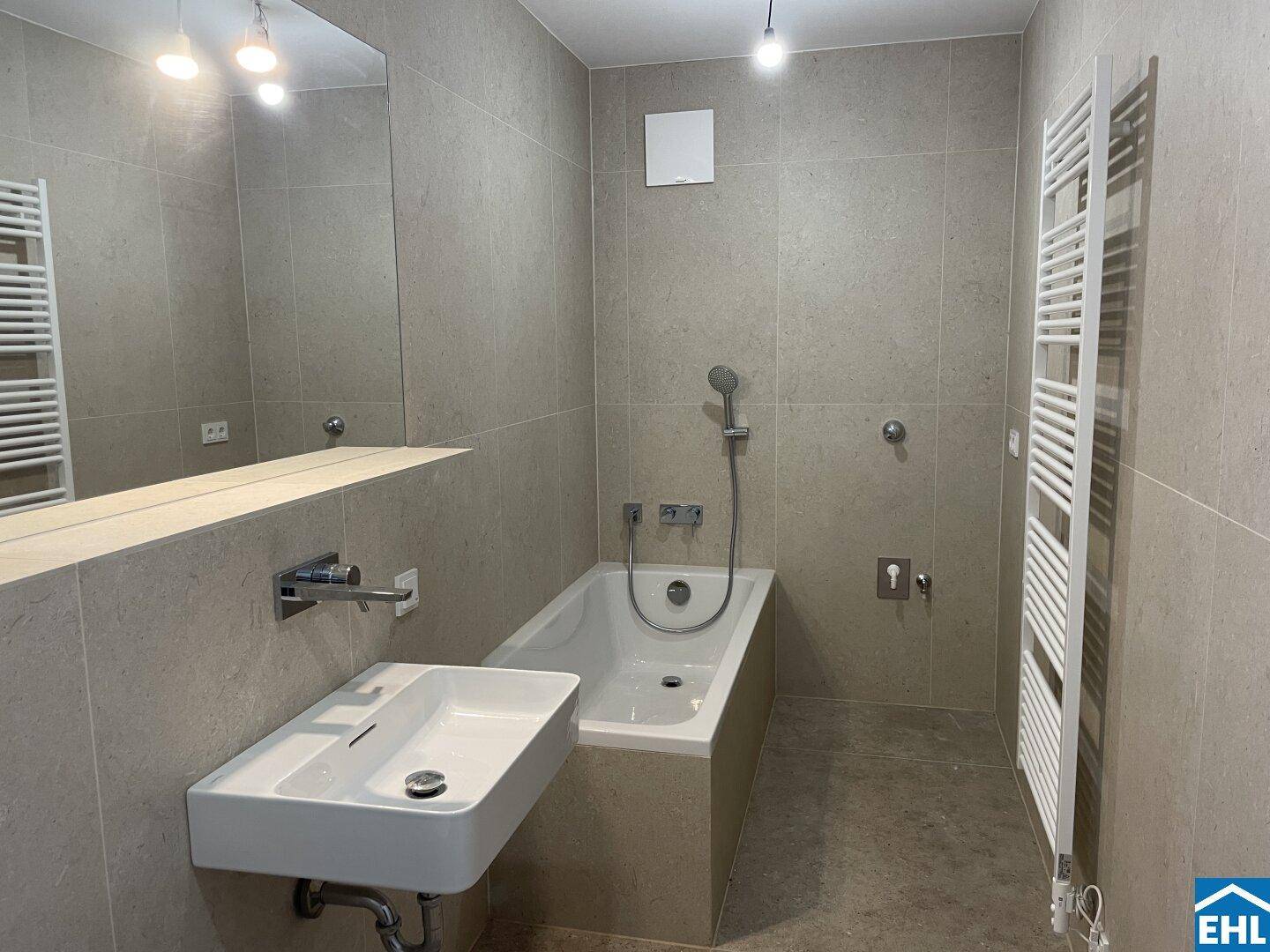 Modernes Badezimmer mit beigefarbenen Fliesen, Badewanne, Waschbecken und beheiztem Handtuchhalter.