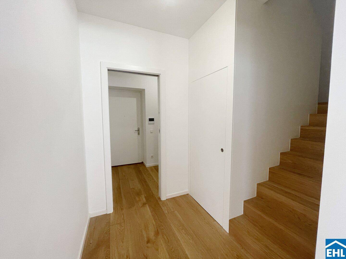 Heller Flur mit Holztreppe und integrierten Schränken, der zu weiteren Räumen führt.