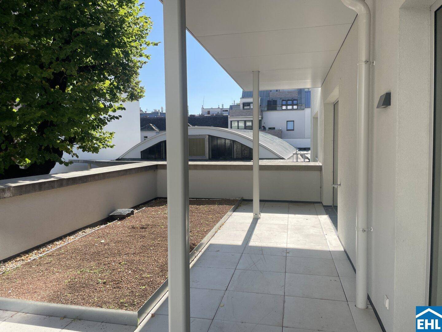 Überdachte Terrasse mit Fliesen und einem kleinen Grünbereich, ideal zum Entspannen.