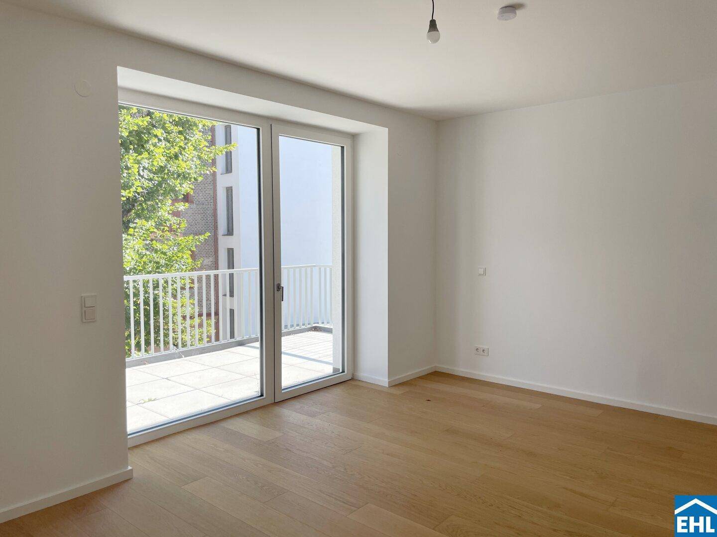 Lichtdurchflutetes Zimmer mit Holzboden und direktem Zugang zu einem großen Balkon.