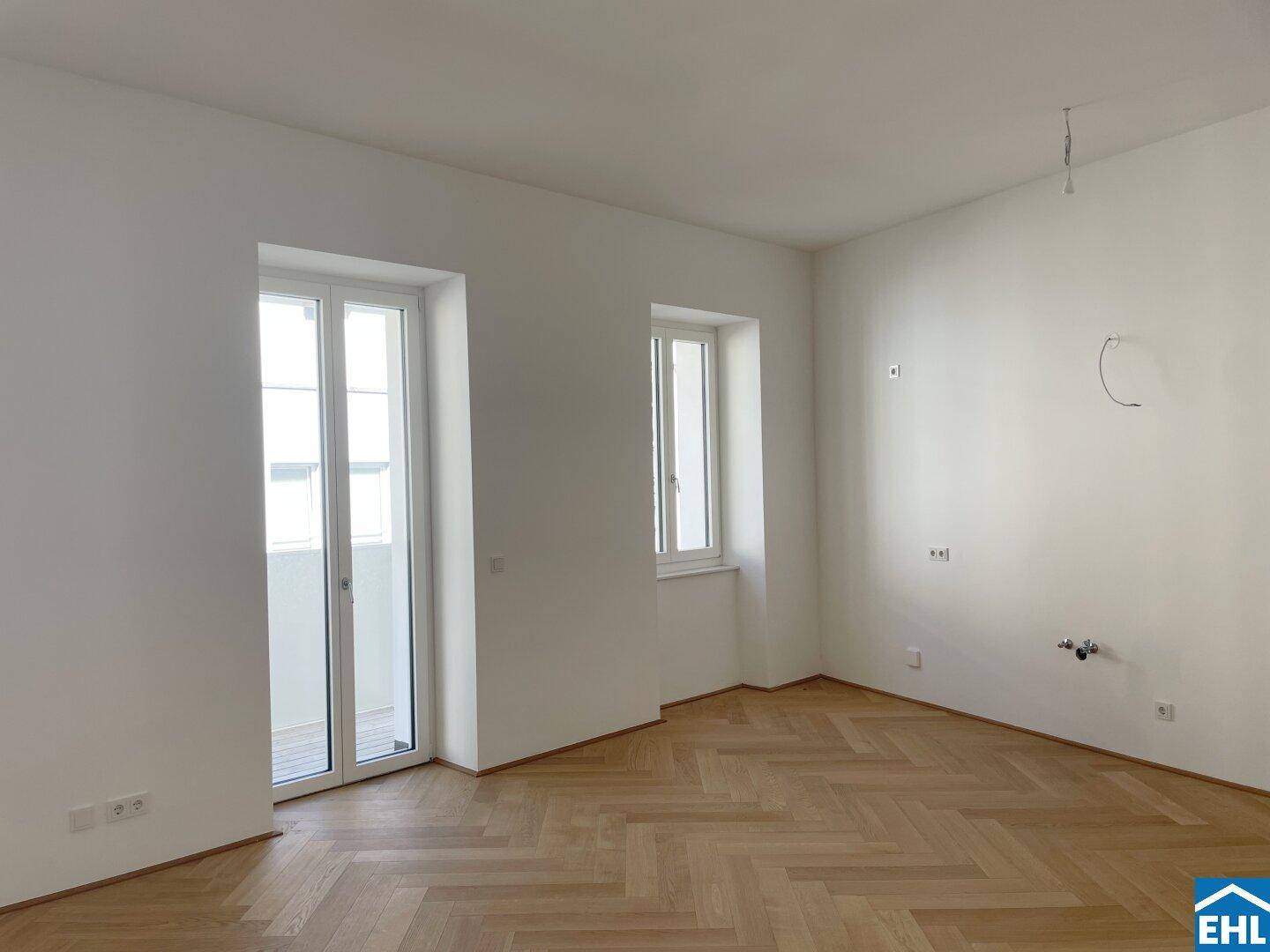 Lichtdurchfluteter Wohnraum mit elegantem Fischgrätparkett und großen Fenstern.