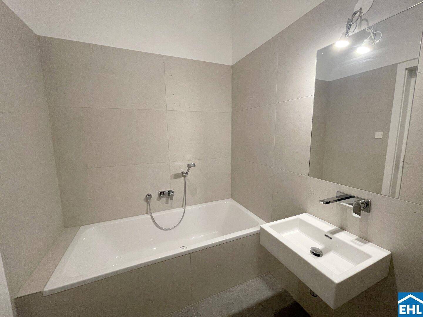 Modernes Badezimmer mit Badewanne, schwebendem Waschbecken und großformatigen Fliesen.