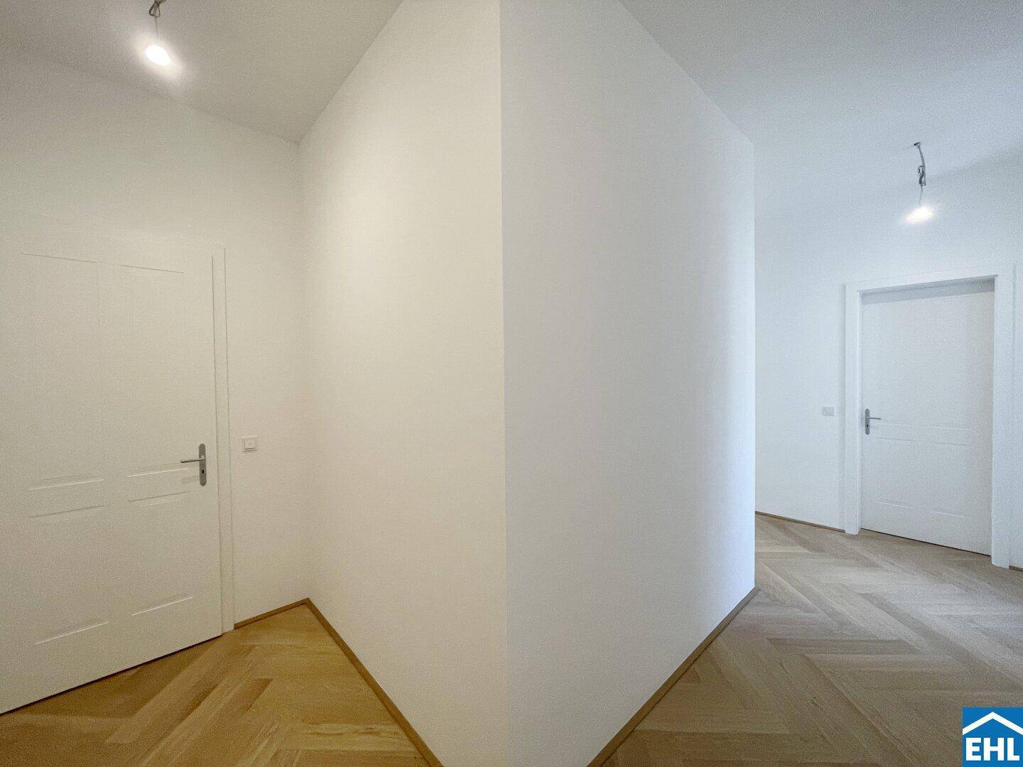 Ecke eines hellen Flurs mit Fischgrätparkett und weißen Türen.