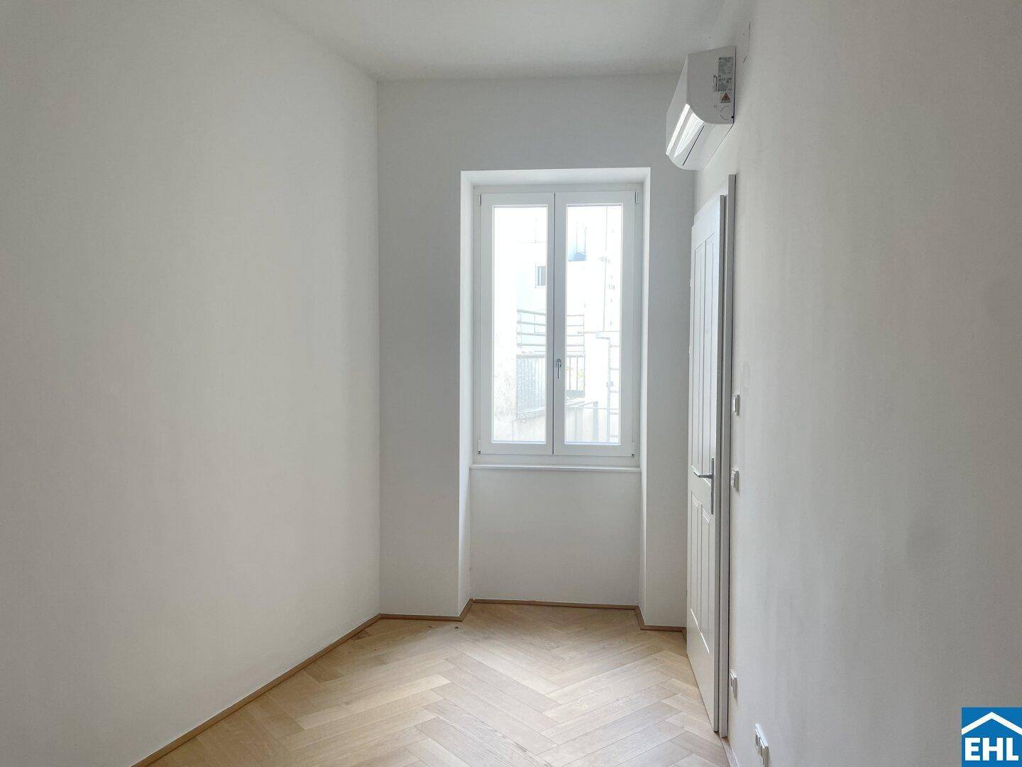 Kleinerer Raum mit Klimaanlage, Fenster und Fischgrätparkett, ideal als Kinderzimmer.