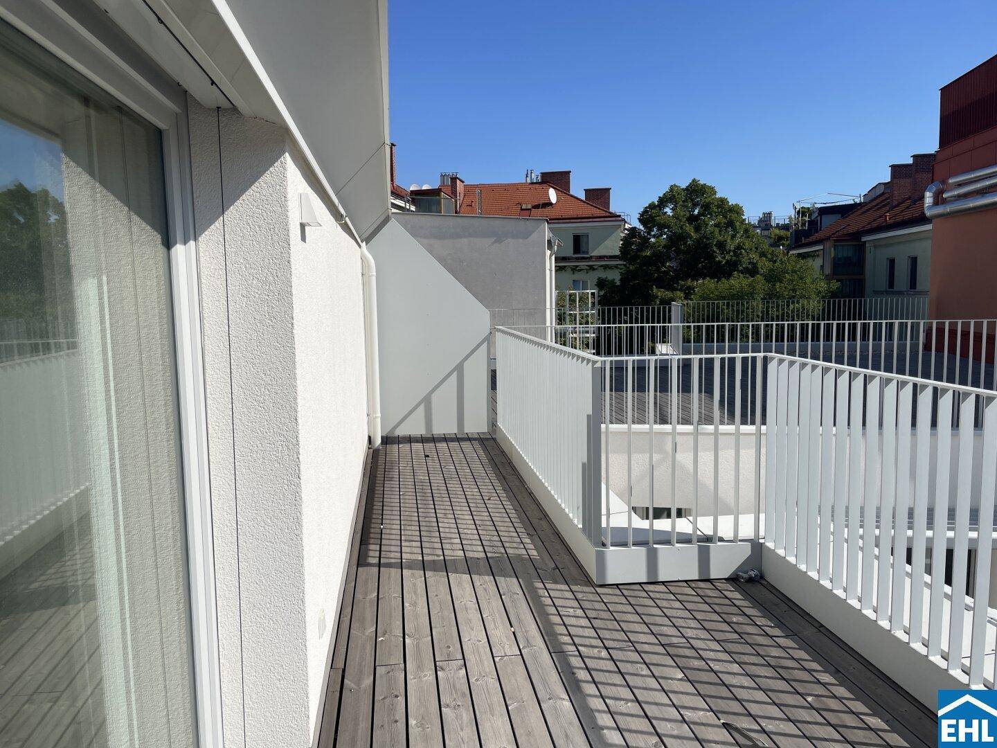 Lange Terrasse mit Holzboden und weißem Geländer, bietet einen angenehmen Blick auf die Umgebung.