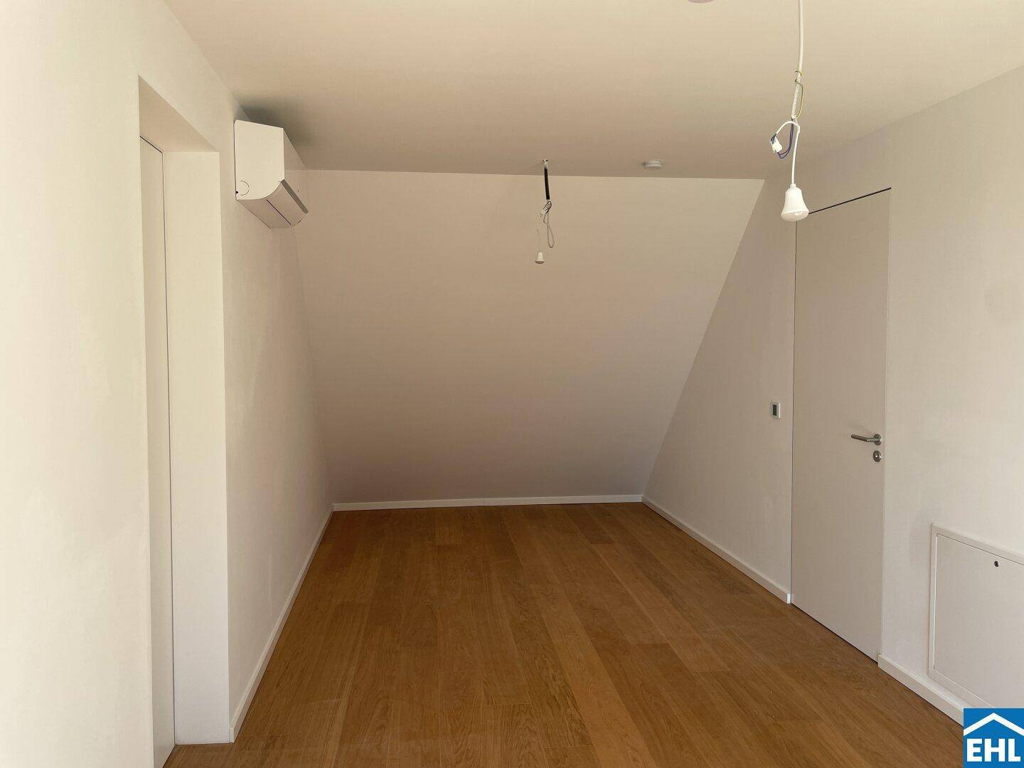 Helles Schlafzimmer mit Holzboden, schrägen Wänden und Klimaanlage, bereit zur individuellen Gestaltung.