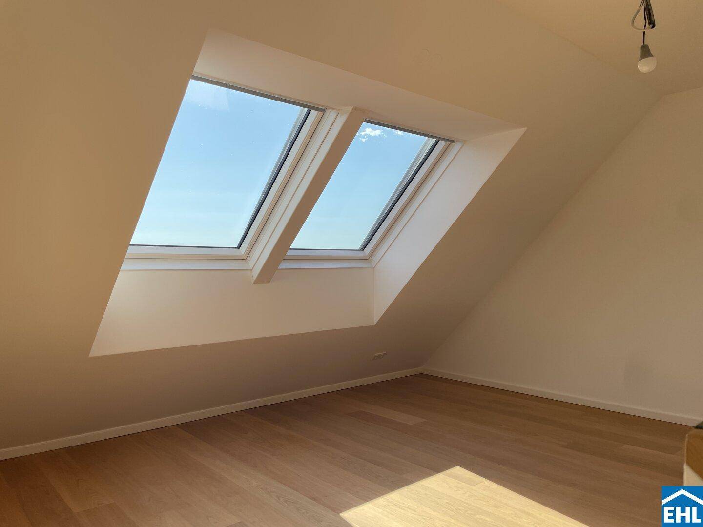 Geräumiges Zimmer mit Holzboden und zwei großen Dachfenstern, die viel Tageslicht hereinlassen.