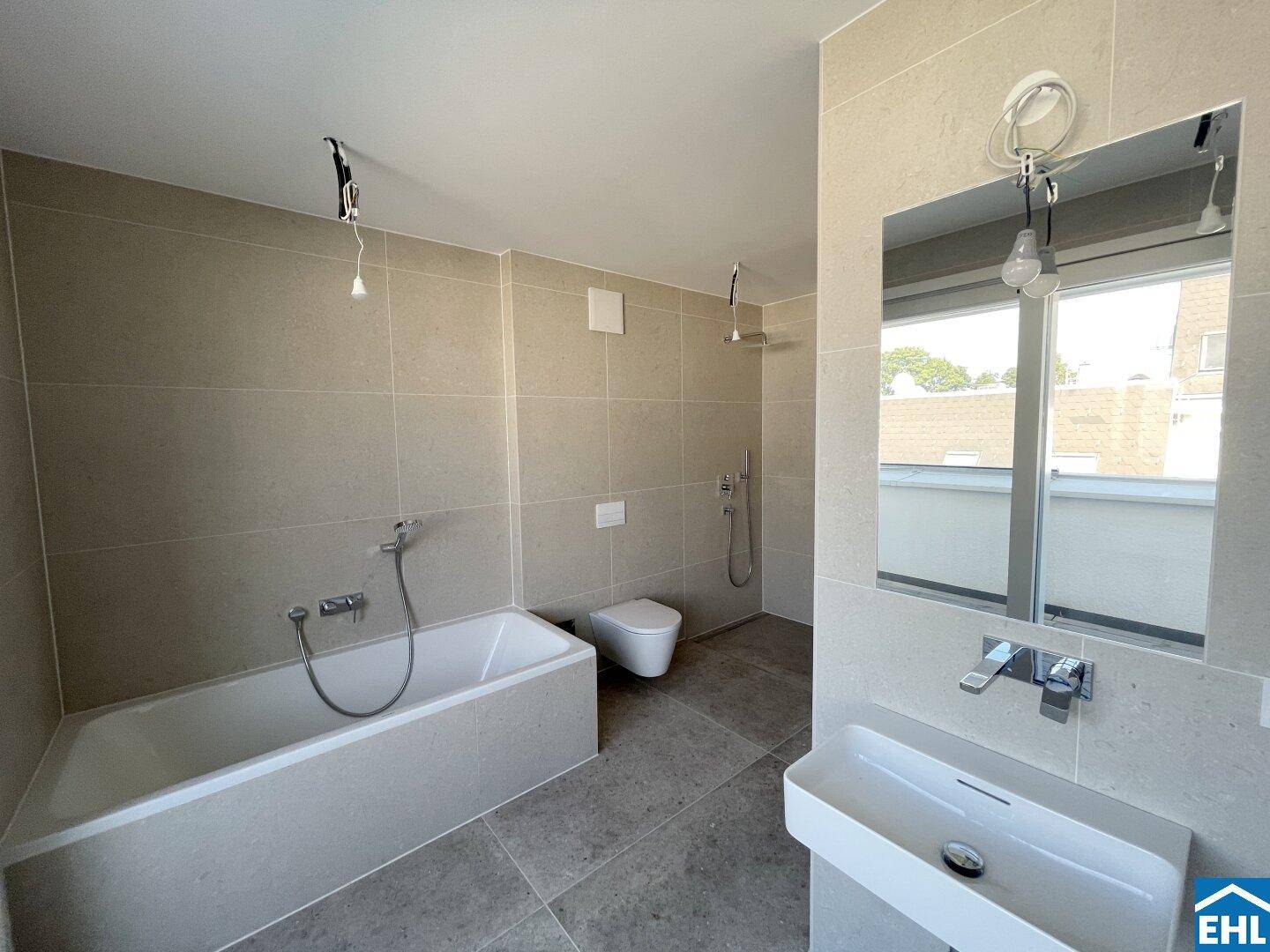 Elegantes Badezimmer mit hellgrauen Fliesen, Badewanne, wandhängendem WC und modernem Waschbecken.