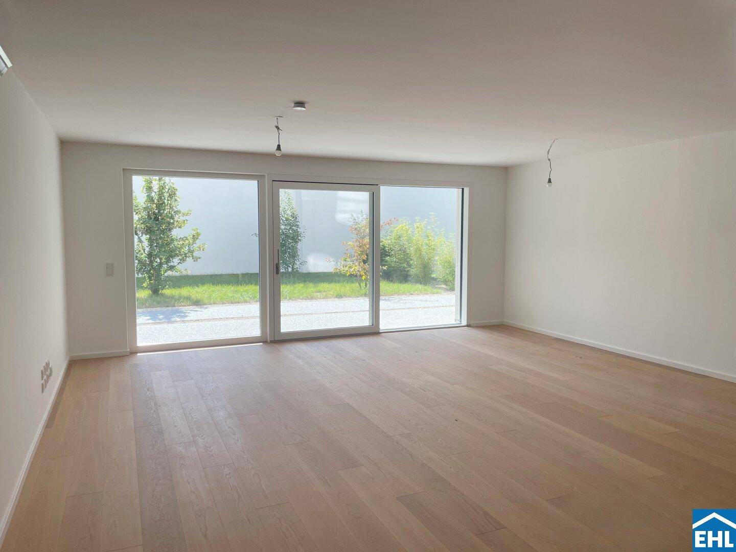 Helles, unmöbliertes Wohnzimmer mit großen Fenstern und hochwertigem Holzparkettboden.