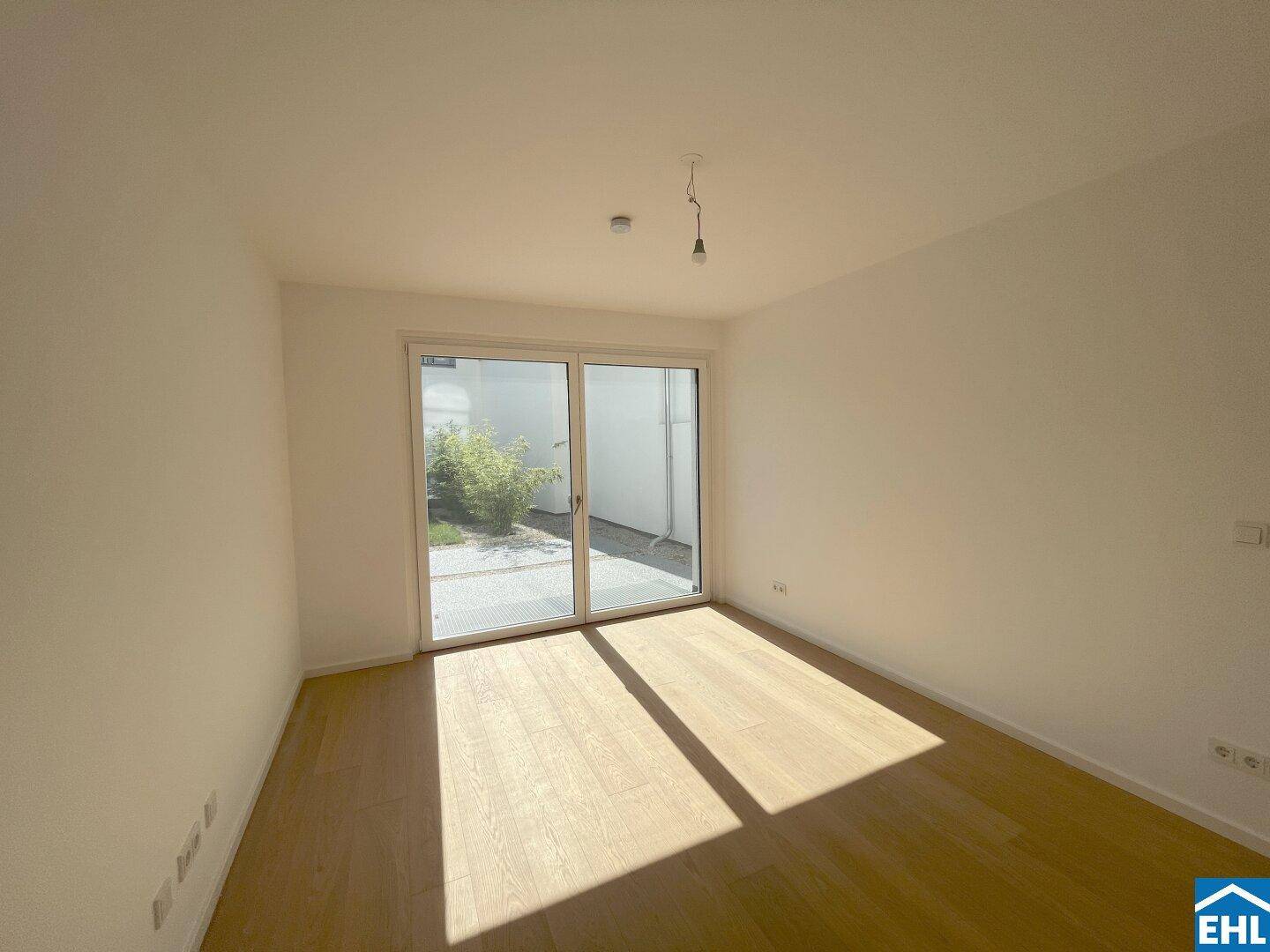 Helles Schlafzimmer mit Holzparkett und Zugang zu einem kleinen Außenbereich durch eine Glasschiebetür.