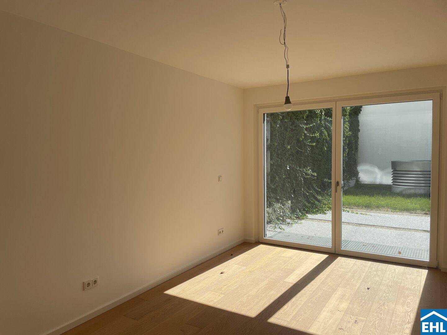 Lichtdurchflutetes Zimmer mit Holzparkett und großem Fenster mit Blick ins Grüne.