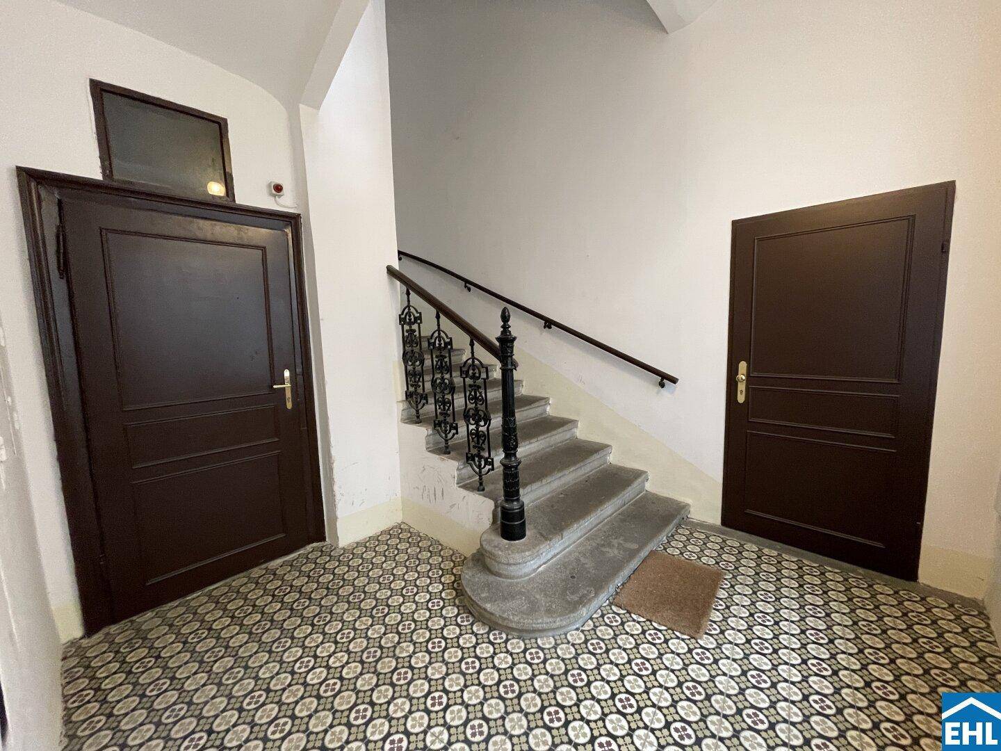 Historisches Treppenhaus mit kunstvollem Geländer, dunklen Holztüren und gemustertem Fliesenboden.