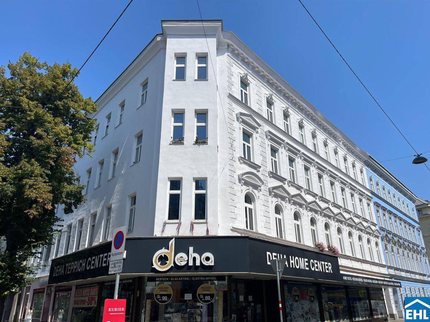 Eckgebäude mit historischer Fassade und Geschäftsflächen im Erdgeschoss unter klarem Himmel.