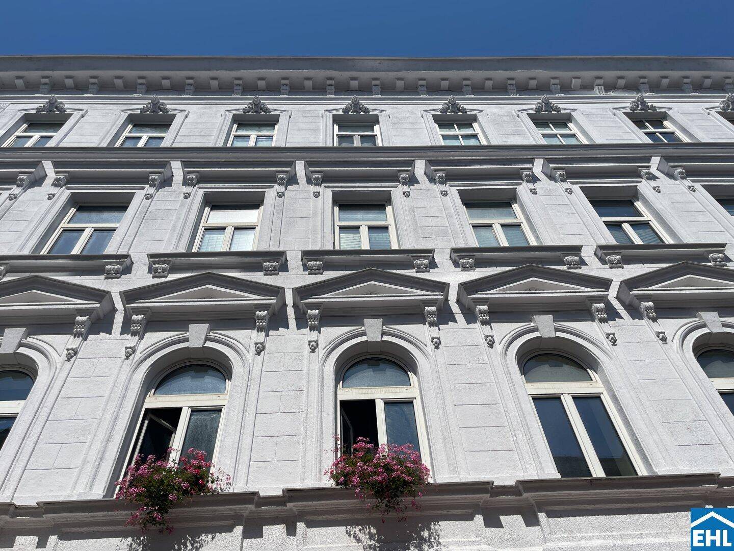 Detailansicht der historischen Fassade mit verzierten Fenstern und Blumenkästen unter blauem Himmel.