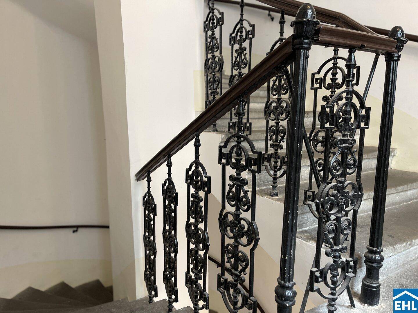 Detailansicht eines kunstvoll geschmiedeten Treppengeländers mit dunklem Holzhandlauf.