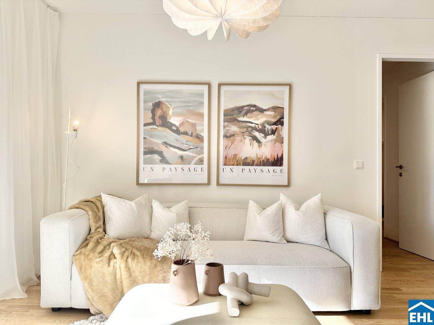 Detailansicht des hellen Wohnzimmers mit beigem Sofa, Kissen und dekorativen Elementen.