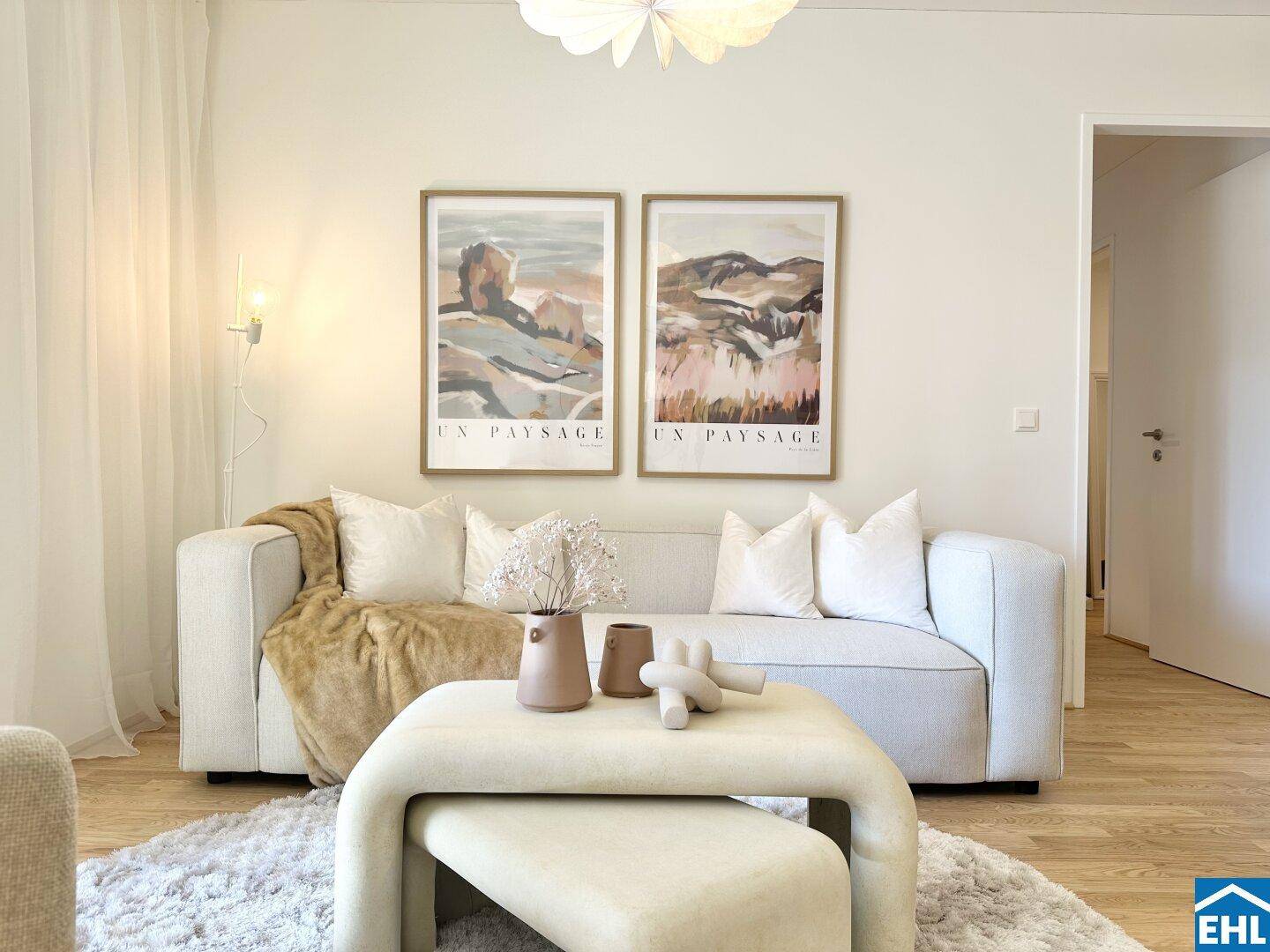 Gemütlicher Wohnbereich mit beigem Sofa, modernem Couchtisch und dekorativen Bildern an der Wand.