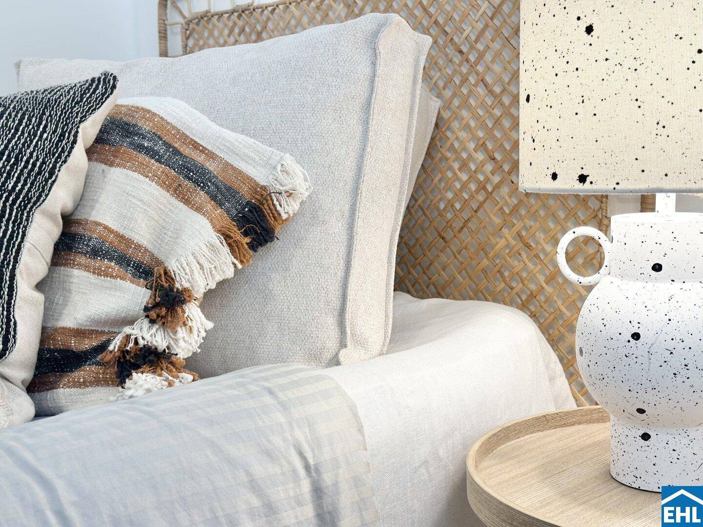 Detailaufnahme eines Bettes mit Rattan-Kopfteil und dekorativen Kissen in warmen Tönen.