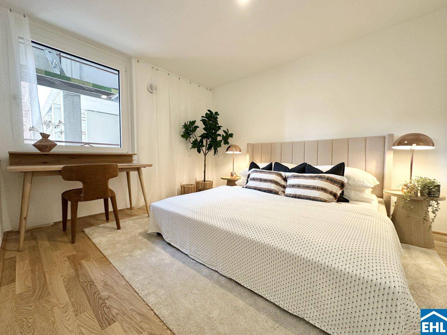 Helles Schlafzimmer mit Doppelbett, Holzboden und einem kleinen Schreibtisch am Fenster.