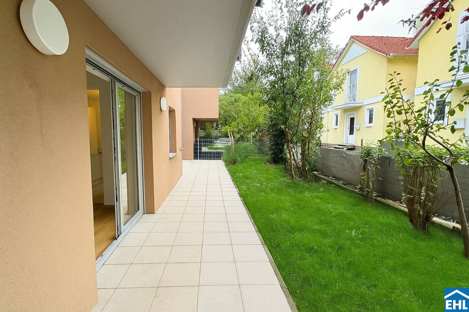 Lange, gepflasterte Terrasse entlang des Hauses mit Rasenfläche und Blick ins Grüne.