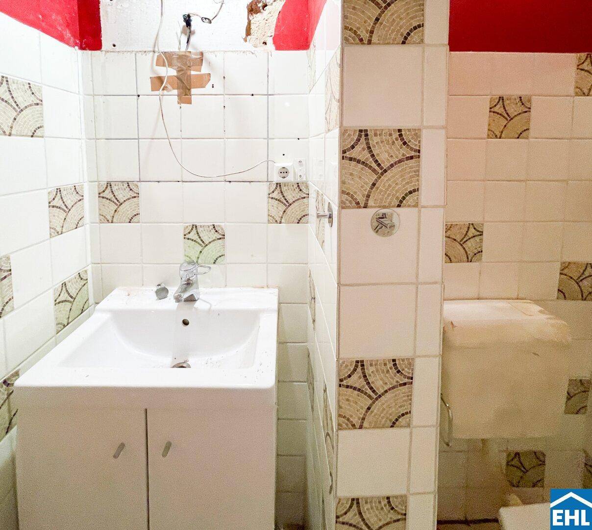 Kleines Badezimmer mit Waschbecken, Fliesen an den Wänden und roten Farbakzenten.