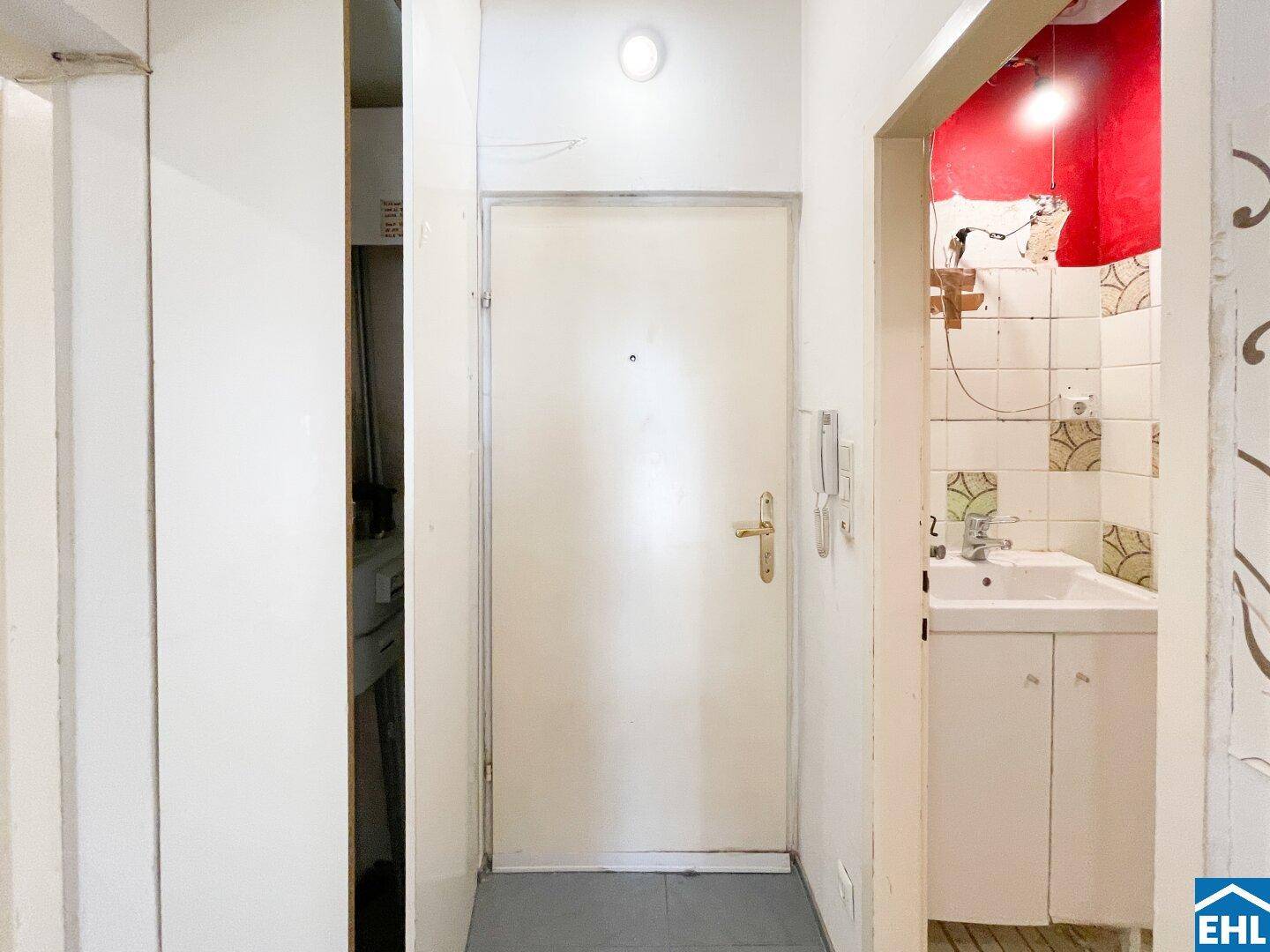 Eingangsbereich mit weißer Tür, Fliesenboden und Blick in ein kleines Badezimmer.
